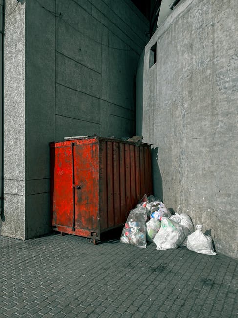 A collection of various plastic storage containers and jerry cans stacked together outdoors on a patch of grass and dirt. The containers are in different bright colors including blue, yellow, red, and